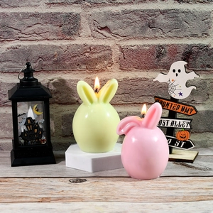 Pastel pink and green bunny Easter candles lit in a cozy rustic holiday setting