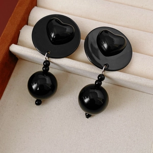 Close-up of black acrylic heart studs with round beaded tassels in a velvet jewelry box