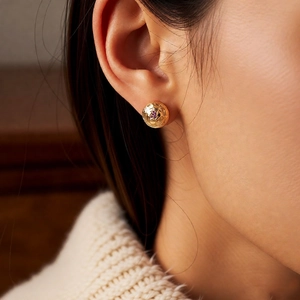 Detail of vintage 18k gold plated round stud earring with ruby on a model wearing a sweater