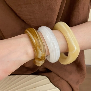 Detail of acrylic cuff bracelets with amber and marble texture patterns on model wrist