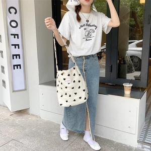 Street style shot of cream canvas tote bag with black heart patterns and woven label