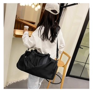 Close-up of a black waterproof travel bag held by a model in a casual indoor setting