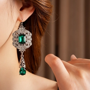 Close-up of vintage emerald teardrop earrings with silver filigree and crystal inlay