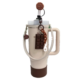 Detail view of Stanley tumbler with chocolate cookie charms and woven strap on beige bottle