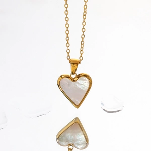 Macro detail of gold heart pendant with white mother of pearl inlay and polished finish