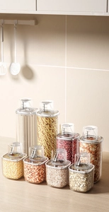 Detail of 8 clear kitchen storage jars with measuring lids on a wooden countertop