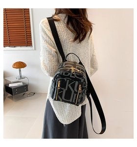 Detail of grey vintage backpack with repeated letter pattern and gold zipper on model