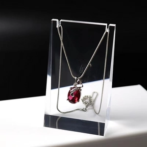 Detail of red oval gemstone pendant on silver chain hanging on acrylic display stand