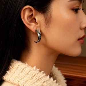 Macro view of C-shaped earrings with colorful gemstones worn by a female model