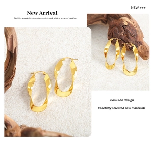 Detailed view of polished gold U-shaped twisted metal hoop earrings on a textured surface