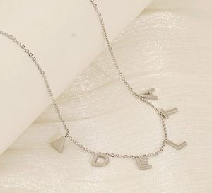 Gros plan d'un collier en acier titane argenté avec des lettres et un pendentif triangle