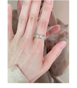 Detailed view of a gold braided bow ring with green and white enamel on a finger