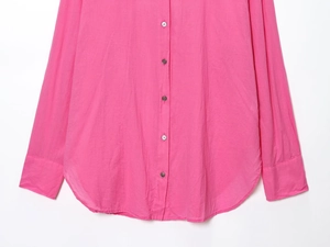 Detailed view of the bright fuchsia button-down shirt featuring fabric pleats and curved hem
