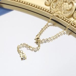 Macro view of gold-plated B-shaped pendant necklace with polished finish on mirror