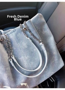 Detailed close-up of light wash denim tote bag with chic metal chain strap on car seat
