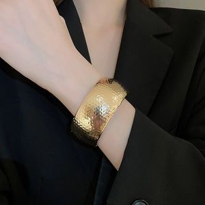 Close-up of a wide golden cuff bracelet featuring a textured hammered metal surface