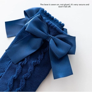 Detail showing high-quality cable knit texture and securely sewn navy satin bows