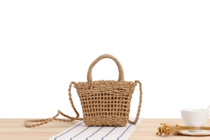 Detail of khaki paper rope woven bag on wooden table with dried flowers and tea cup