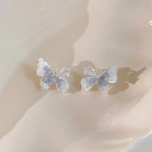 Vue macro des boucles d'oreilles papillon argentées avec cristaux bleus sur fond beige