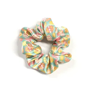Detail of mint green satin scrunchie featuring colorful Easter egg patterns and soft texture