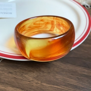 Detail of amber acrylic bangle with marble patterns on a vintage ceramic plate