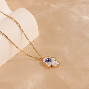 Macro shot of gold Hamsa pendant with white crystals and blue heart on silk background