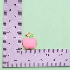 Detail showing pink apple fruit pendant with gold metal edges and green leaf on ruler
