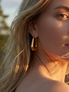 Polished gold U-shaped geometric hoop earring worn by a model in warm outdoor lighting