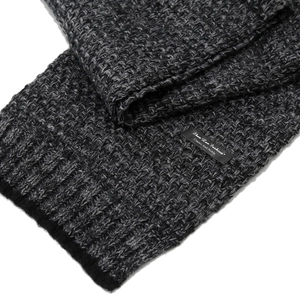 Close-up of thick grey knitted scarf showing ribbed texture and black fabric brand label