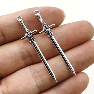Pair of silver sword alloy pendants for DIY jewelry being held against white background