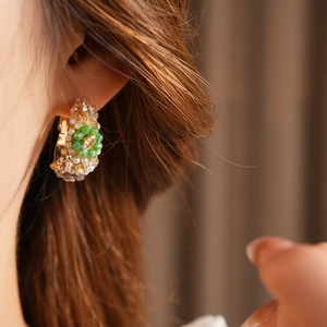 Close-up of vintage gold hoop earring with green beads and faux pearls on model