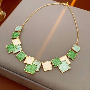 Détail de pendentifs carrés en émail émeraude et crème sur un collier doré