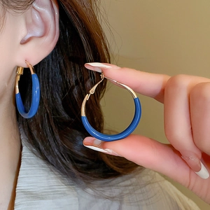 Detailed close-up of Klein blue enamel and gold metal hoop earrings on ear