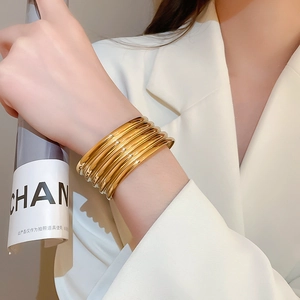 Detail of layered golden stainless steel bangles with polished finish on model's wrist