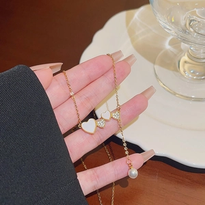Gold heart pearl necklace featuring heart pendants and a pearl drop in a stylish closeup