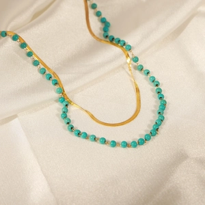 Double layer gold snake chain and turquoise bead necklace on white silk background