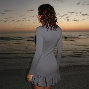 Robe moulante grise à manches longues et volants sur la plage au coucher du soleil