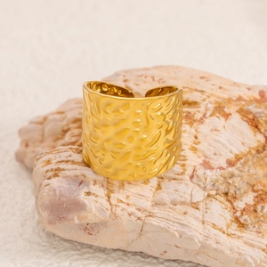 Macro shot of wide gold-plated stainless steel ring with hammered texture on rock