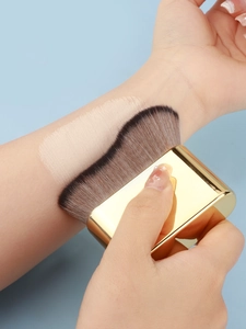 Macro shot of wavy foundation brush applying seamless liquid makeup on skin with gold handle