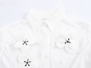 Close-up of white textured shirt featuring 3D floral appliqués and pearl button details