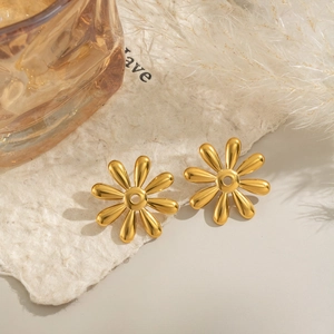 Elegant 18k gold floral earrings on a textured beige background with feathers
