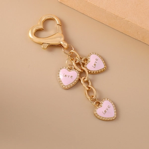 Golden heart keychain with pink enamel Love pendants on a minimalist beige background