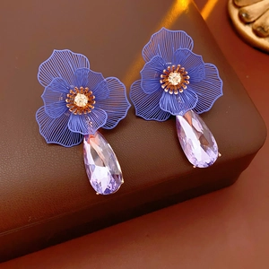 Detail of flower stud earrings with purple teardrop crystal on brown leather background