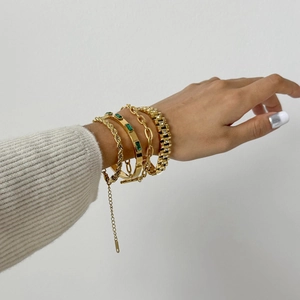 Detailansicht goldener Armbänder mit Kordelkette und Smaragd-Armreif am Handgelenk