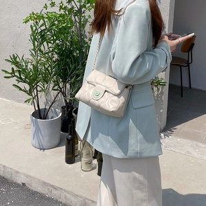 Detail of a beige quilted crossbody bag with metal chain strap in an outdoor setting