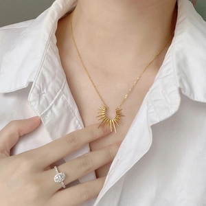 Golden sunburst pendant necklace and silver oval diamond ring on model in white shirt