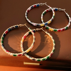 Close-up of gold and silver hoop earrings with rainbow square zircon on leather surface