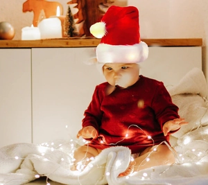 Close-up of a plush LED Christmas hat worn by a baby among warm festive holiday lights