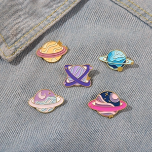 Detail of five colorful enamel planet pins scattered on blue denim fabric background