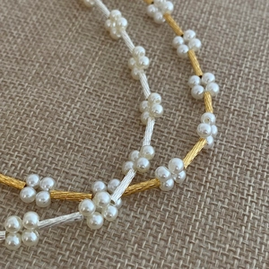 Macro detail of elegant pearl flower design with textured metallic tubes on gold necklace